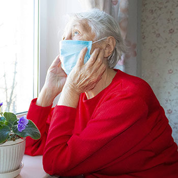 Photo d'une personne âgée portant un masque et regardant par la fenêtre de manière pensive